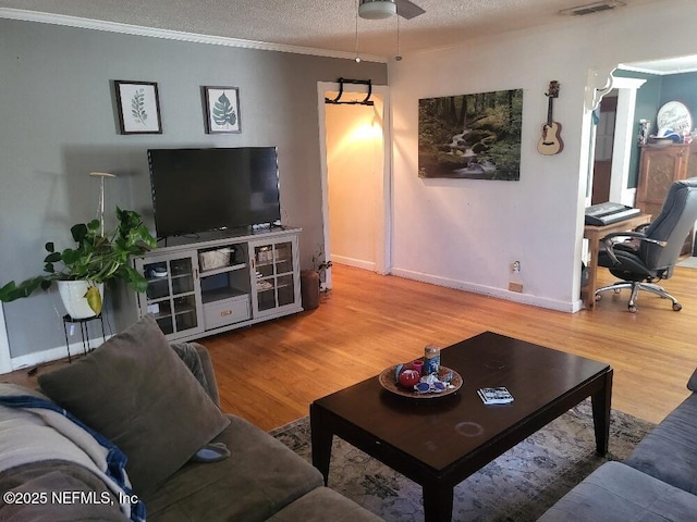 living room with wood finished floors, visible vents, baseboards, ornamental molding, and a textured ceiling