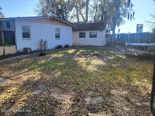 back of property with concrete block siding, fence, central air condition unit, a trampoline, and a lawn