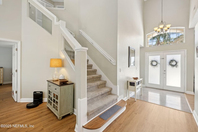 foyer entrance featuring a notable chandelier, stairway, light wood finished floors, baseboards, and a towering ceiling