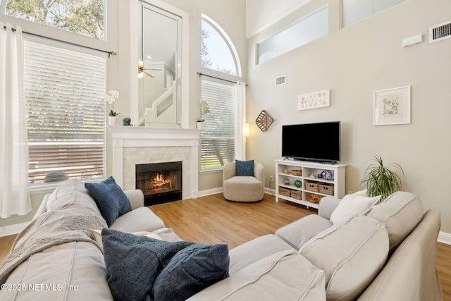 living room with wood finished floors, visible vents, a high ceiling, ceiling fan, and a tiled fireplace