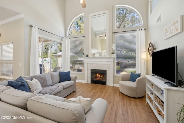 living room featuring baseboards, ceiling fan, a fireplace, a high ceiling, and wood finished floors