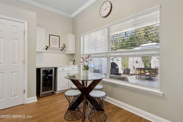 dining space with light wood-type flooring, beverage cooler, crown molding, and a dry bar