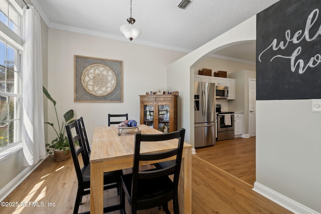 dining area featuring arched walkways, a healthy amount of sunlight, crown molding, and light wood-type flooring