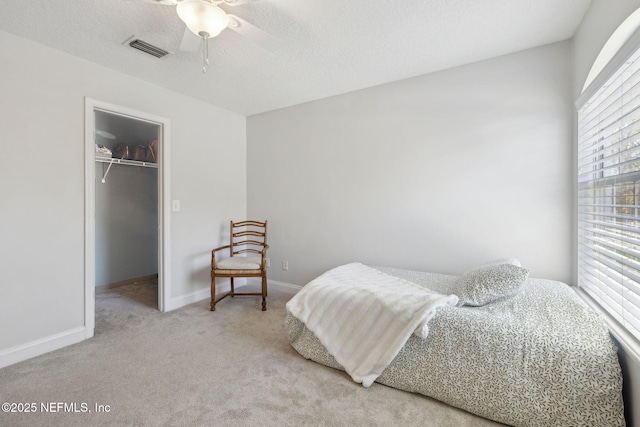 bedroom with visible vents, a closet, a textured ceiling, a walk in closet, and carpet flooring