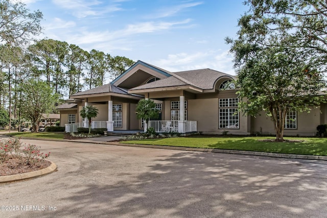 view of front facade with covered porch, curved driveway, and a front lawn