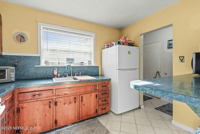 kitchen featuring light tile patterned floors, brown cabinetry, a toaster, freestanding refrigerator, and a sink