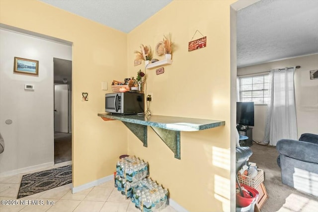 kitchen featuring tile patterned floors, stainless steel microwave, baseboards, and a textured ceiling