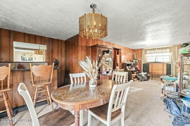 carpeted dining space featuring a chandelier, a textured ceiling, and wood walls