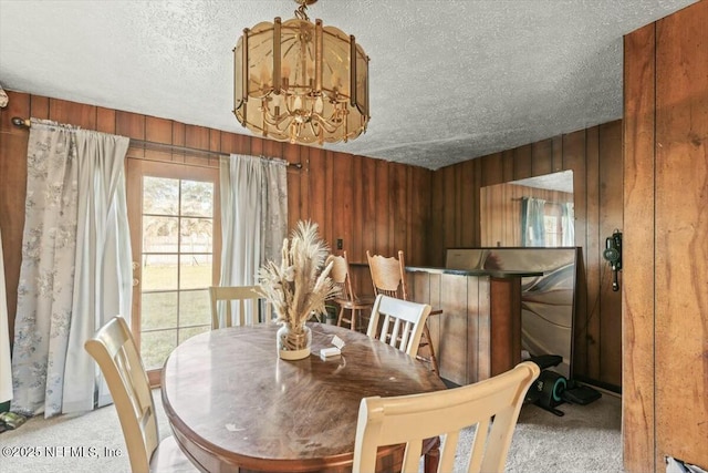 dining area featuring a chandelier, light colored carpet, wood walls, and a textured ceiling