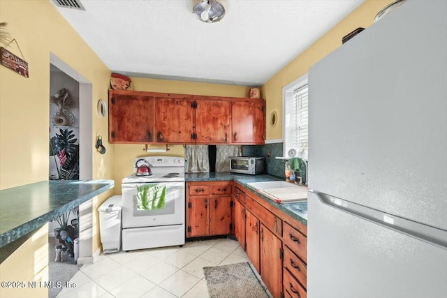 kitchen featuring dark countertops, backsplash, light tile patterned floors, white appliances, and a sink