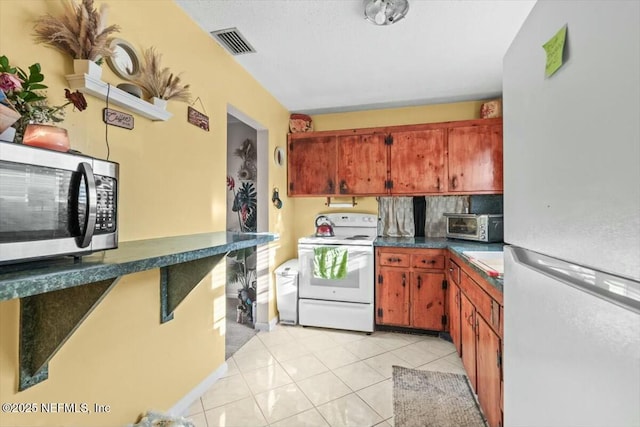 kitchen featuring white appliances, light tile patterned floors, visible vents, dark countertops, and brown cabinets