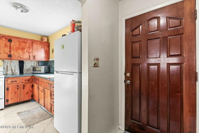 kitchen with light tile patterned floors, brown cabinetry, freestanding refrigerator, stove, and tasteful backsplash