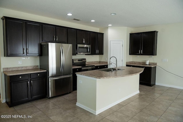 kitchen with a sink, a kitchen island with sink, dark cabinets, and stainless steel appliances