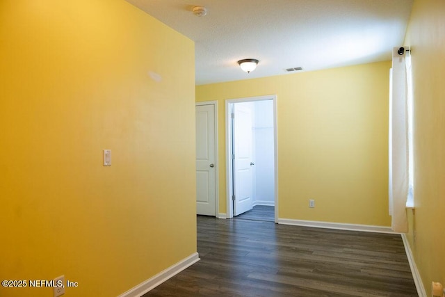 unfurnished room featuring dark wood finished floors, visible vents, and baseboards