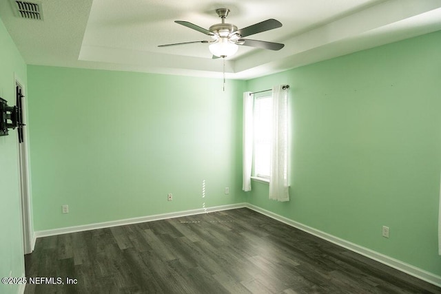 unfurnished room with visible vents, ceiling fan, baseboards, a tray ceiling, and dark wood-style floors