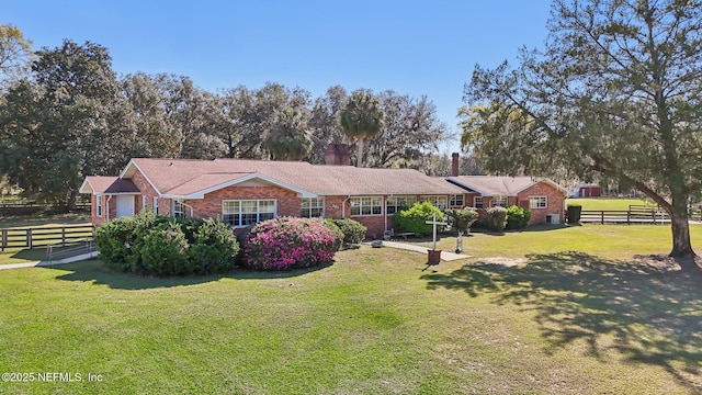 ranch-style house featuring brick siding, roof with shingles, a front lawn, and fence