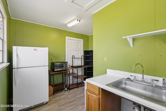 kitchen with light wood-type flooring, a sink, freestanding refrigerator, a toaster, and light countertops