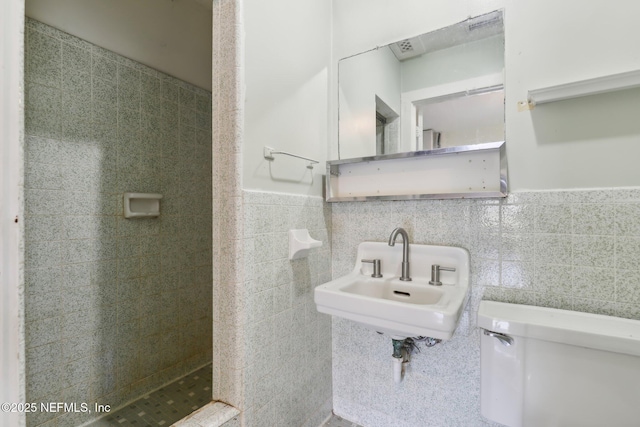 full bath with tiled shower, a sink, wainscoting, tile walls, and toilet