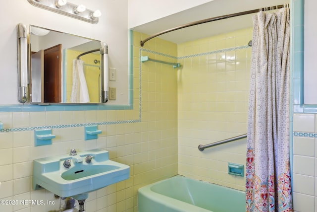 bathroom with shower / bath combo with shower curtain, tile walls, and a sink