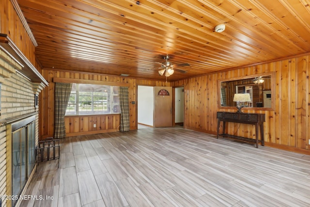 unfurnished living room with a fireplace, wood finished floors, wooden walls, and a ceiling fan