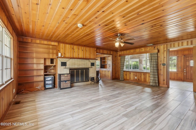 unfurnished living room with built in shelves, wooden ceiling, wood walls, a fireplace, and ceiling fan