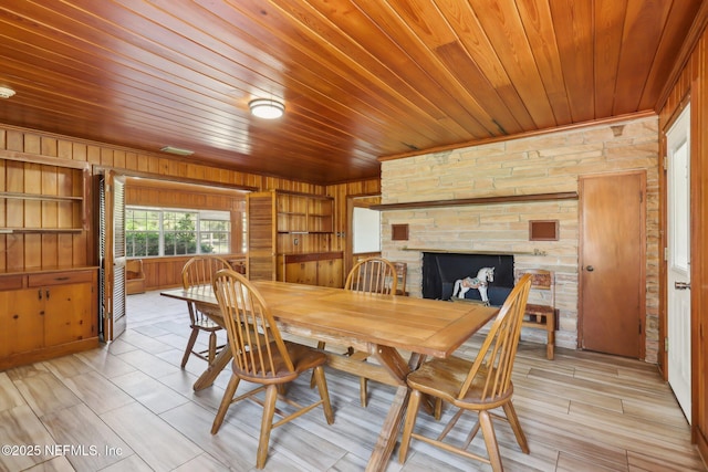 dining space featuring a stone fireplace, wooden walls, built in shelves, and wood ceiling