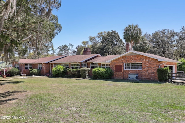 view of front of property with brick siding, a chimney, a front lawn, and fence