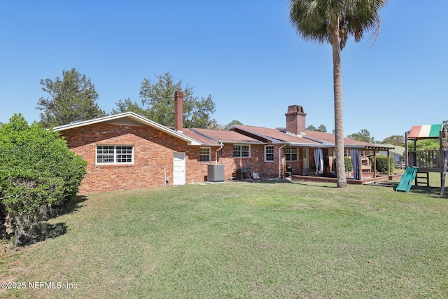 rear view of property featuring a playground, a yard, cooling unit, brick siding, and a chimney