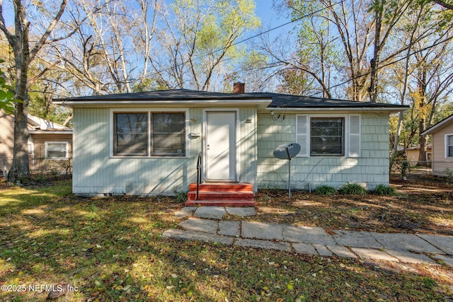 bungalow-style house with a front yard, entry steps, a chimney, and fence