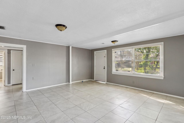 empty room featuring light tile patterned floors, visible vents, a textured ceiling, and baseboards