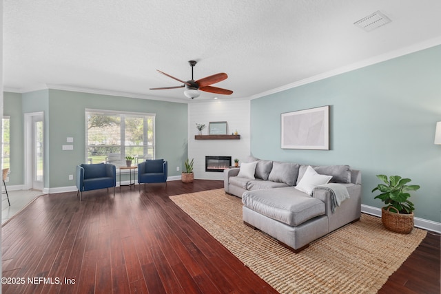 living area featuring visible vents, dark wood-type flooring, ornamental molding, a large fireplace, and baseboards