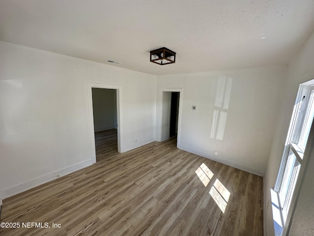 spare room featuring visible vents, light wood-style floors, baseboards, and a textured ceiling