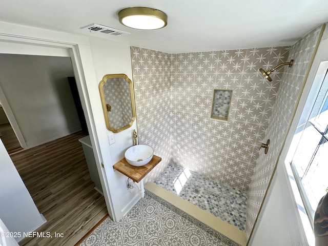 full bathroom with wood finished floors, baseboards, visible vents, a tile shower, and a sink