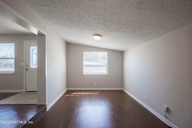 empty room with a wealth of natural light, a textured ceiling, baseboards, and wood finished floors