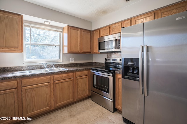 kitchen with a sink, dark countertops, appliances with stainless steel finishes, and brown cabinetry