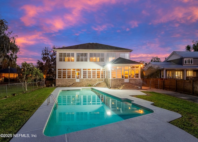 back of house at dusk featuring a patio, a yard, a fenced backyard, and stone siding