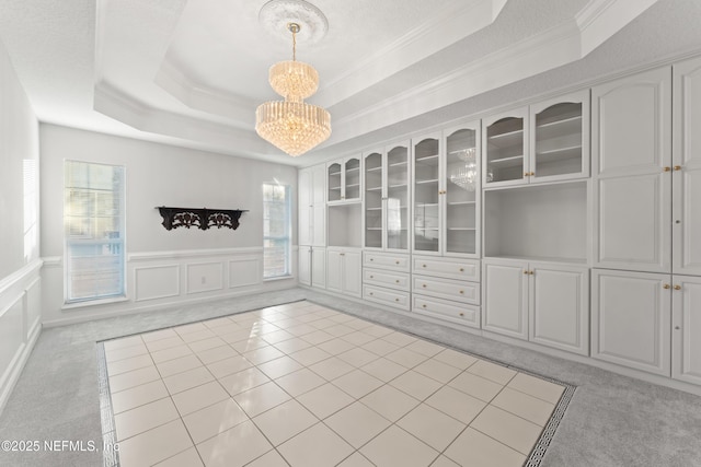 spare room featuring wainscoting, a raised ceiling, a decorative wall, light colored carpet, and a chandelier