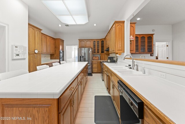 kitchen featuring recessed lighting, a sink, stainless steel appliances, glass insert cabinets, and a center island