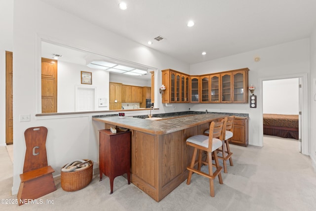 kitchen featuring light carpet, a breakfast bar, recessed lighting, brown cabinetry, and glass insert cabinets