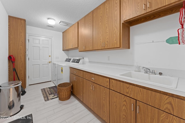 washroom featuring visible vents, washer and clothes dryer, a sink, a textured ceiling, and cabinet space