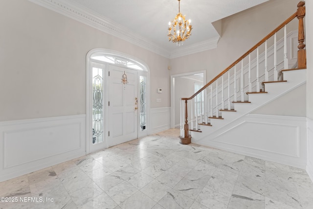 entrance foyer with a chandelier, a wainscoted wall, stairs, ornamental molding, and marble finish floor