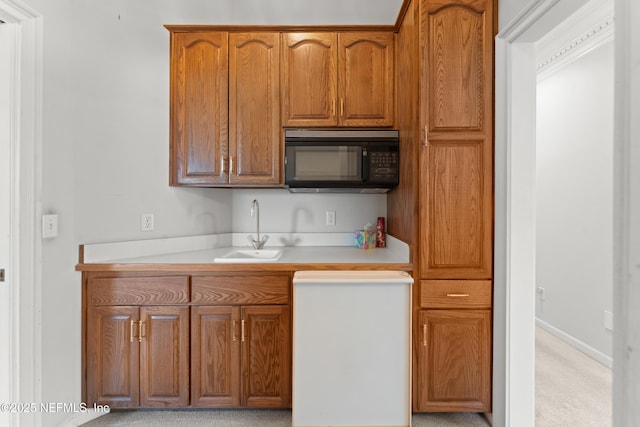 kitchen featuring baseboards, black microwave, light countertops, brown cabinets, and a sink