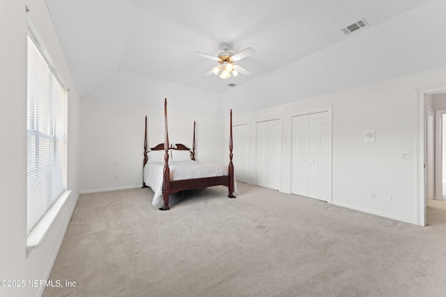 unfurnished bedroom featuring visible vents, baseboards, carpet, multiple closets, and vaulted ceiling