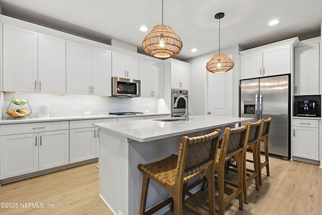 kitchen with a sink, stainless steel appliances, light wood-style floors, and backsplash