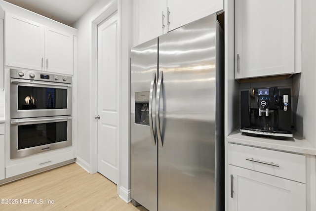 kitchen with stainless steel appliances, decorative backsplash, light countertops, light wood-style floors, and white cabinetry