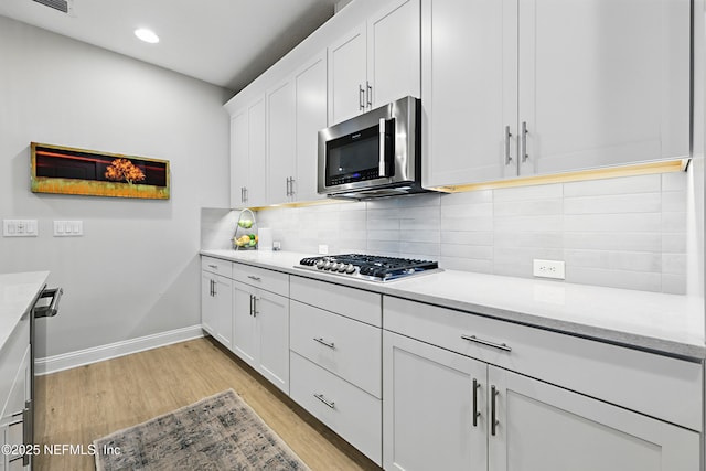 kitchen featuring light countertops, decorative backsplash, light wood-style flooring, appliances with stainless steel finishes, and white cabinets