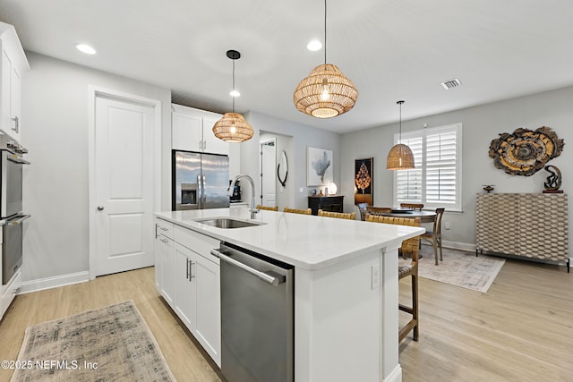 kitchen featuring a sink, light wood-type flooring, white cabinets, stainless steel appliances, and a kitchen island with sink