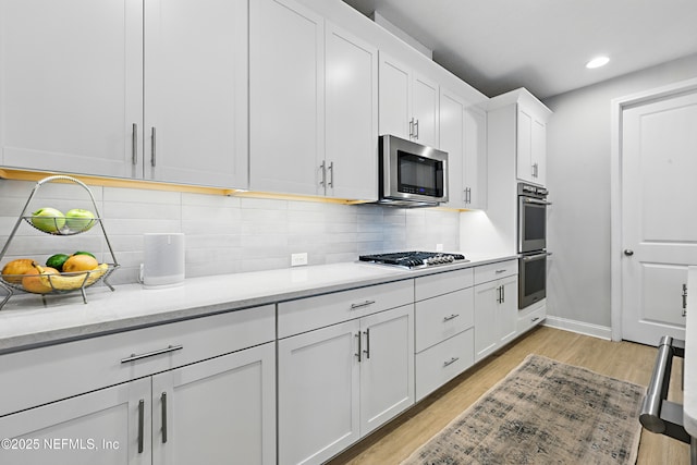 kitchen featuring baseboards, light wood finished floors, stainless steel appliances, white cabinetry, and tasteful backsplash