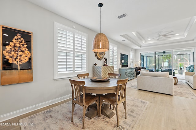 dining area with visible vents, a raised ceiling, wood finished floors, and a ceiling fan