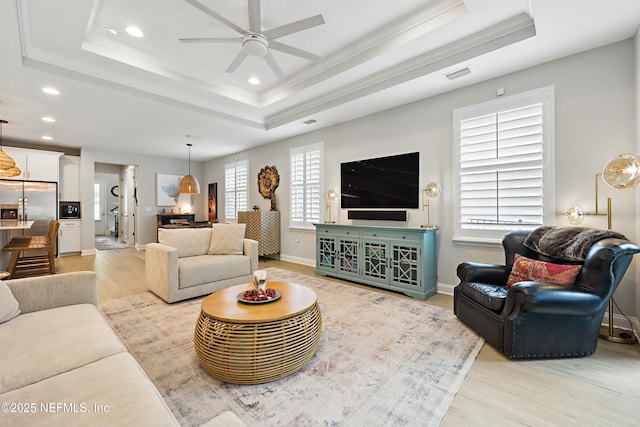 living room featuring light wood finished floors, a ceiling fan, and a tray ceiling